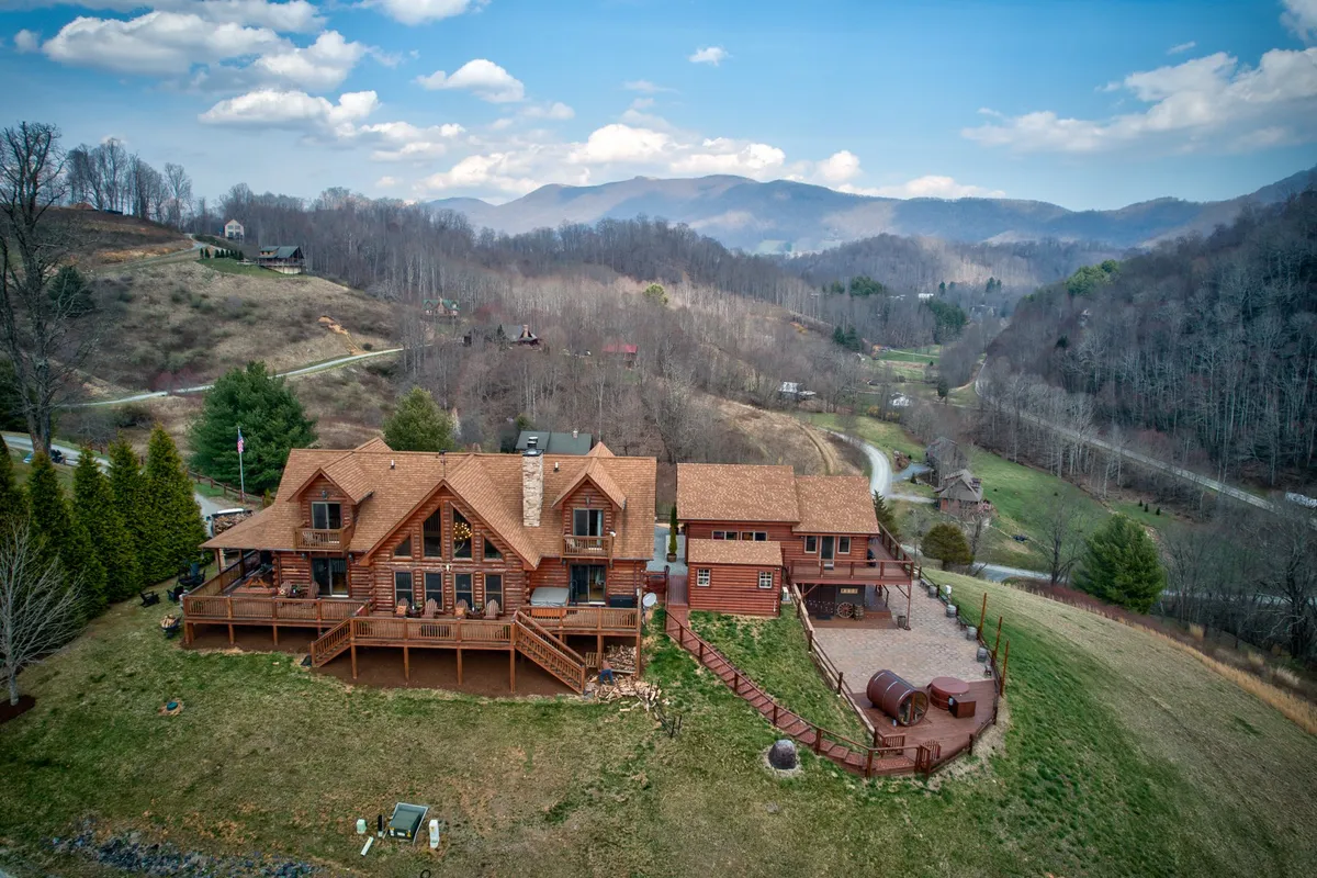 This exterior shot features the log cabin's distinctive architecture nestled against a backdrop of sweeping mountain vistas. The spacious deck, landscaped yard, and the surrounding natural beauty are prominent, inviting guests to imagine relaxing outdoors or setting off on a High Country adventure.