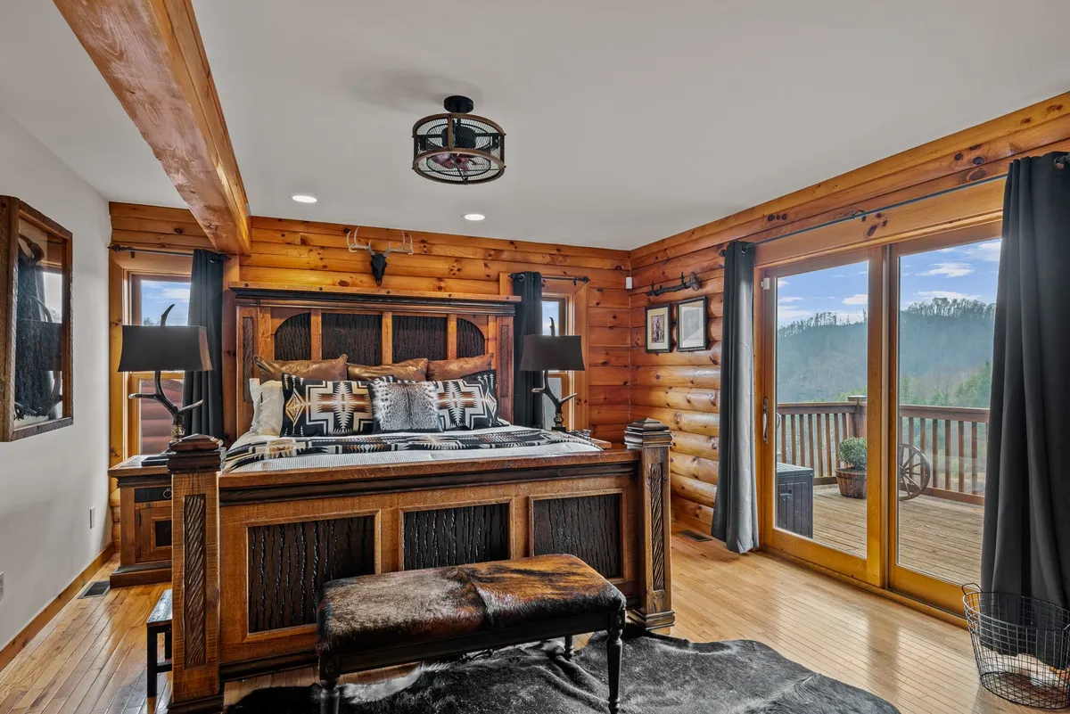 A cozy bedroom suite with a wooden bed frame, decorative pillows, and large windows that open up to scenic views. Warm lighting from lamps on bedside tables enhances the tranquil and welcoming ambiance.