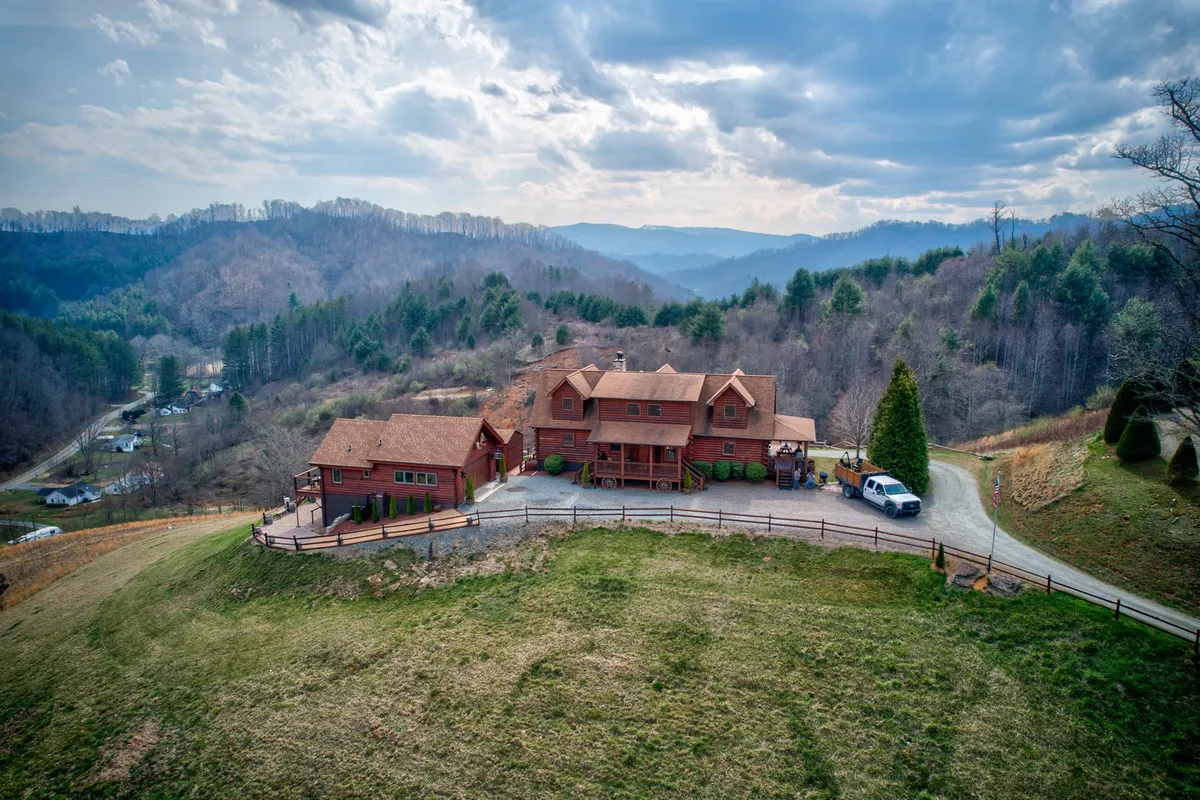 A large red house sits amidst rolling mountains, with a winding driveway leading through lush greenery. The natural setting hints at nearby trails and seasonal foliage, embodying the spirit of high country adventures and accessibility to outdoor recreation.