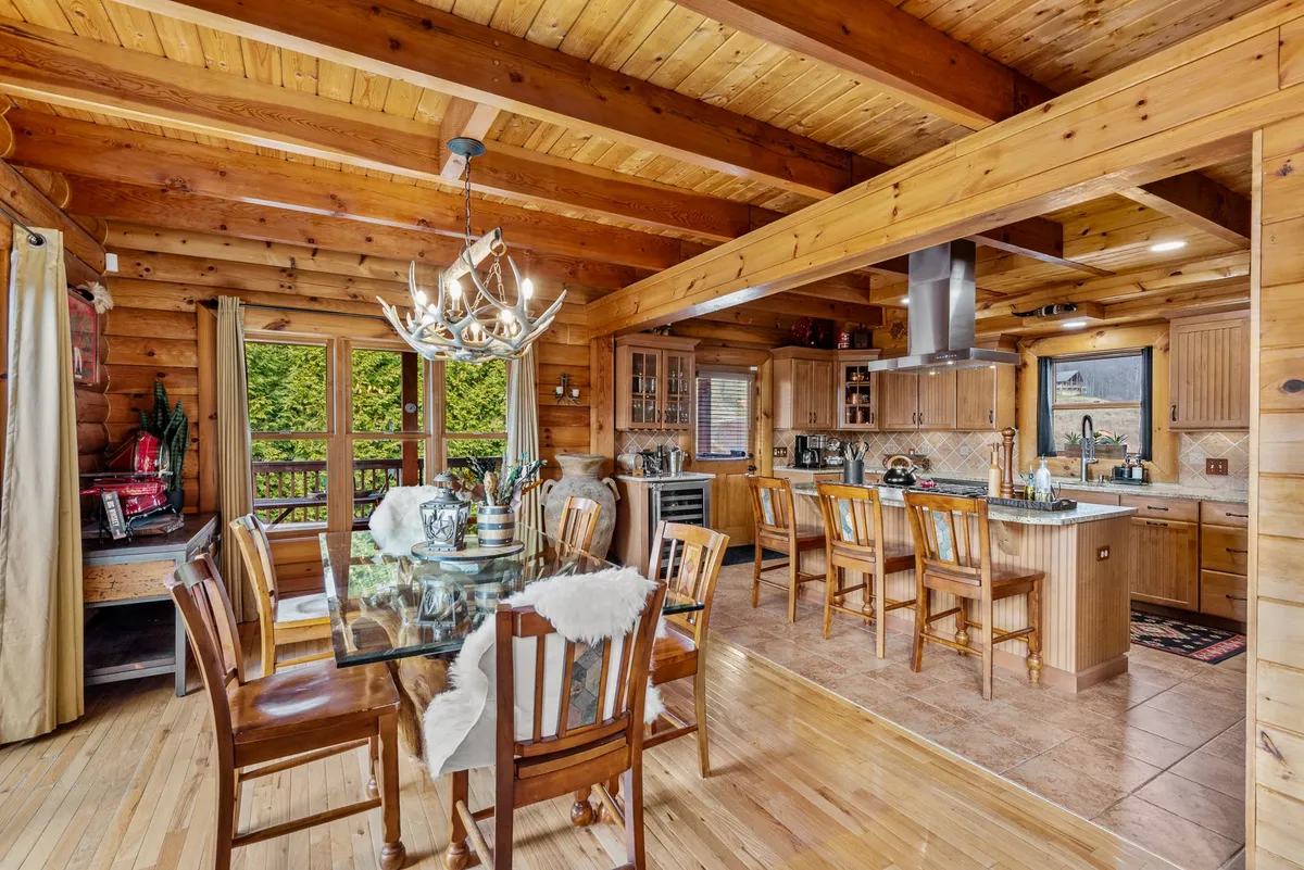 A chef-inspired kitchen and adjacent dining area, featuring a generous wooden dining table under a rustic chandelier, a central kitchen island, and cabinetry in warm tones. The area is designed for family meals and entertaining, with a welcoming, communal vibe.