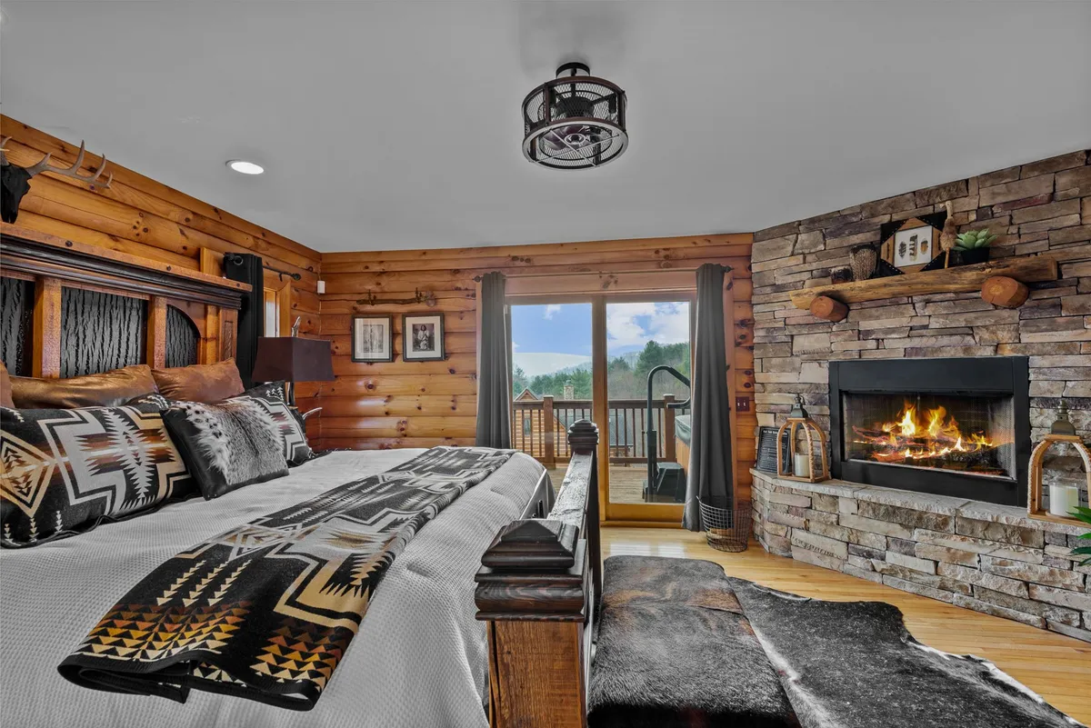 A spacious bedroom featuring a plush bed, a crackling fireplace, a sliding door to the outside, and tasteful decorative accents. The setting feels both luxurious and homey, perfect for unwinding after a day of adventure.