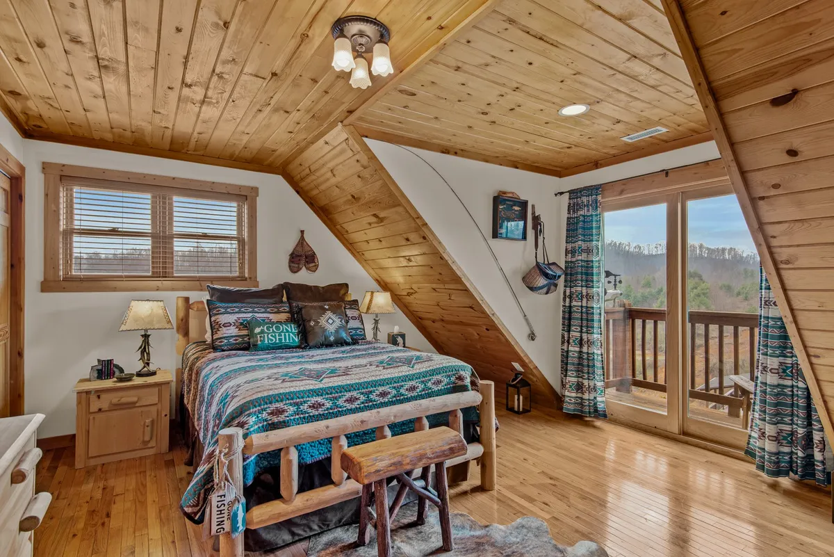 A serene bedroom with a bed dressed in patterned bedding, wooden furniture, and expansive windows that offer picturesque views. The space is flooded with natural light and exudes peacefulness.