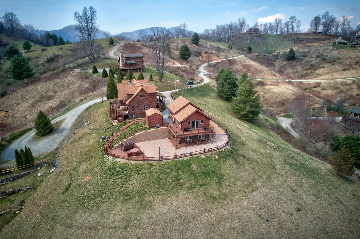 This image captures two large wooden cabins surrounded by lush greenery and a mountain backdrop. A winding driveway leads up to the homes, and the tranquil scene highlights the property's expansive and private layout perfect for large groups and family gatherings.