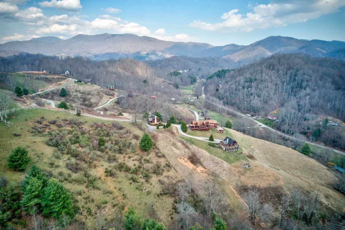 An expansive landscape view featuring rolling hills, scattered cabins, and winding roads weaving through lush greenery. The perspective invokes a sense of exploration and connection to the local area, hinting at the nearby scenic trails perfect for morning walks or afternoon breaks.