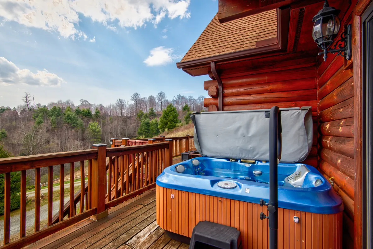 A serene wooden deck with a hot tub overlooks a beautifully wooded landscape. The setting feels private and peaceful, ideal for soaking after a day exploring the mountains, and highlights the integration of wellness features with nature.