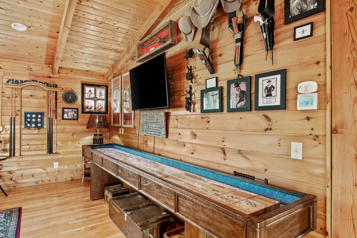This image presents a long wooden table surrounded by rustic decor, including mounted guns, framed photographs, a wall clock, and decorative hats. The setup evokes a sense of camaraderie and nostalgia, hinting at memorable gatherings, game nights, and storytelling sessions.
