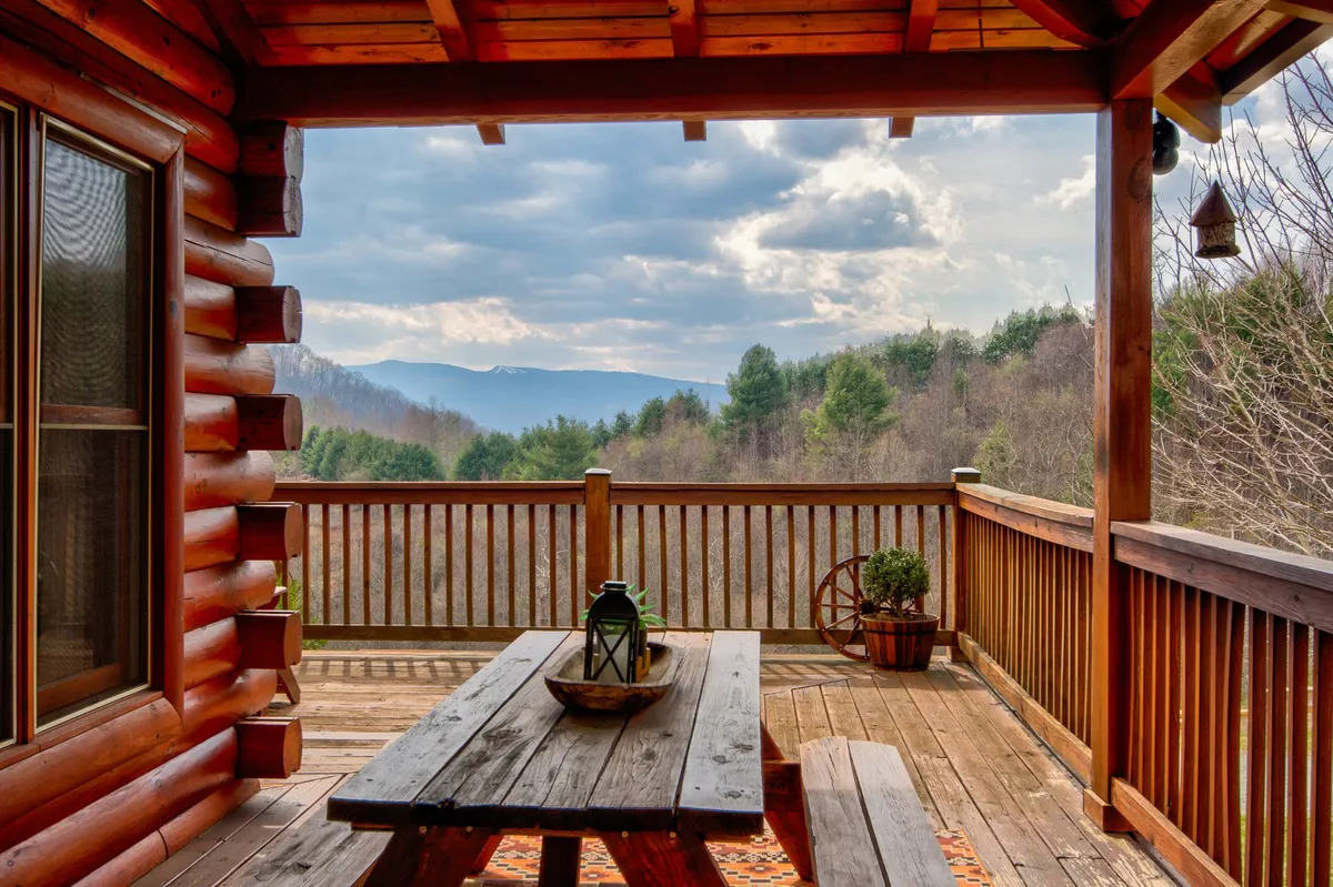An inviting outdoor picnic area featuring a sturdy wooden table with a stunning mountain view. Lanterns and a decorative bowl add warmth, while the serene landscape invites relaxation and group outdoor meals.