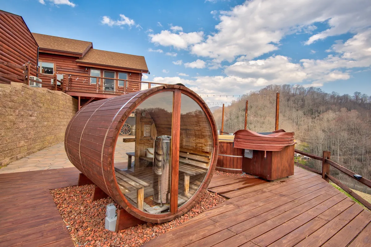 An inviting exterior scene showing a barrel sauna and bubbling hot tub on a wooden deck, surrounded by tranquil landscapes. The setup hints at relaxation after outdoor adventures, with mountains and nature as a backdrop.