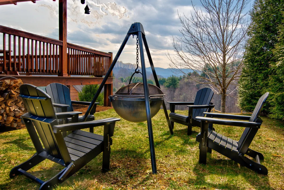 A cozy fire pit area surrounded by Adirondack chairs and a wooden deck, with a stack of firewood ready for evening gatherings. The setup invites groups to relax, share stories, and enjoy the peaceful outdoors.