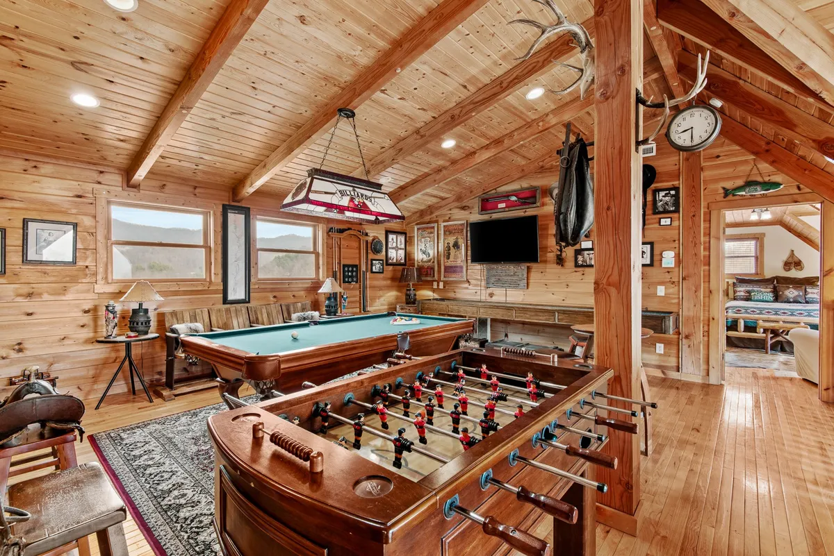 This image captures the loft game room with a pool table and foosball table as focal points. The space features wooden beams, antler decor, and wall art, creating a playful and relaxed atmosphere ideal for entertainment. Ample seating and open sightlines are visible, reinforcing the area’s suitability for group gatherings and game nights.
